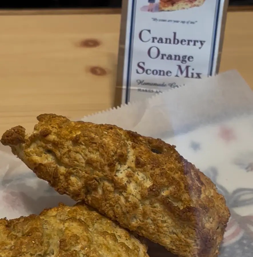 Fresh-baked cranberry orange scones on parchment, beside a bag of Martha's Cranberry Orange Scone Mix